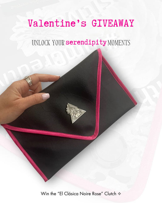 Hand holding a black clutch with pink trim, promotional text for a Valentine's Day giveaway. Black envelope clutch bag with pink trim and silver triangle logo; El Clásica Noire Rose clutch by t•Ana Couture displayed on a light background.