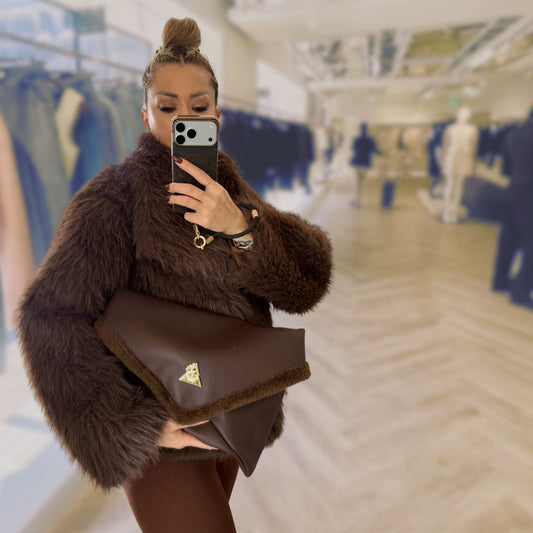 The Amara Duo from t•Ana Couture’s Chocolate Edit features two luxury multi wear clutch bags; one Grande and one Petite; designed to be worn together or individually. Crafted in plush chocolate brown faux fur and finished with gold logo hardware, the Amara bags bring warmth, texture and refined slow luxury to any look. Each piece can be styled as a clutch, shoulder bag or crossbody, offering versatile day to evening wear. Here we see the grande, larger spacious bag.