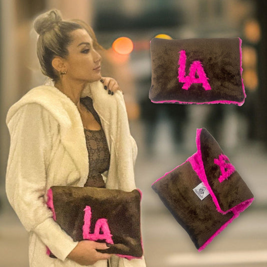 t•Ana Couture LA SnugglePlush Elegante handbag in brown faux fur with bold pink plush trim and LA lettering; luxury statement clutch styled with cream coat; sustainable upcycled design with modern street-luxe elegance.