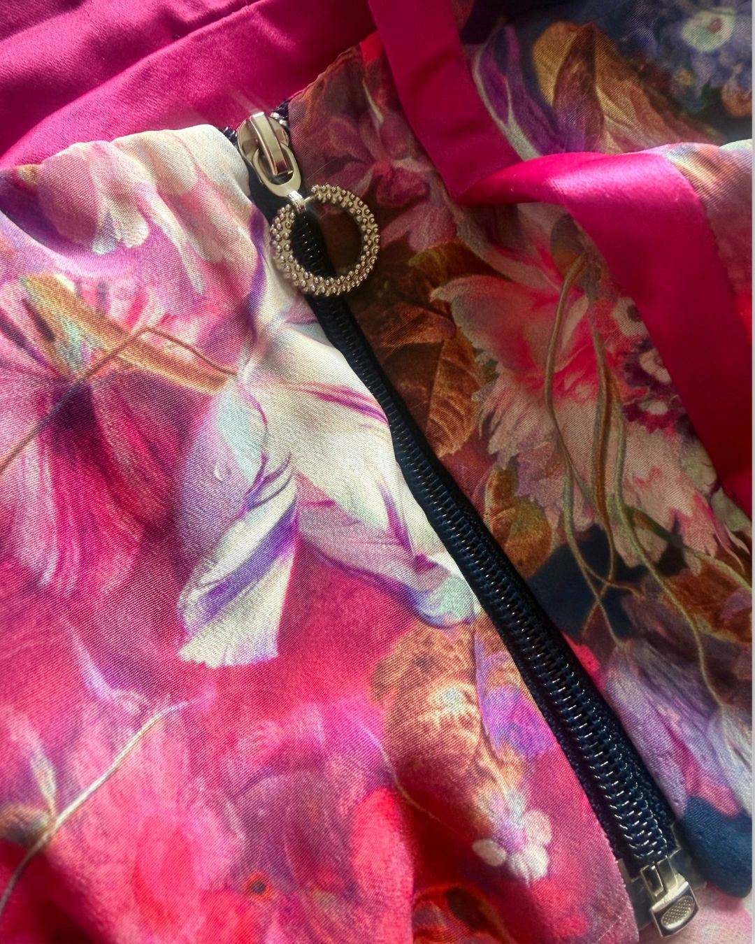 Luxury details of High-quality floral fabric detail showing print and texture of couture three-piece set; a floral satin couture set in blush and fuchsia tones by t•Ana Couture; captured under Mediterranean sunlight with divine flow and effortless elegance. Close up of luxury zipper with crystal ring puller on couture floral garment.