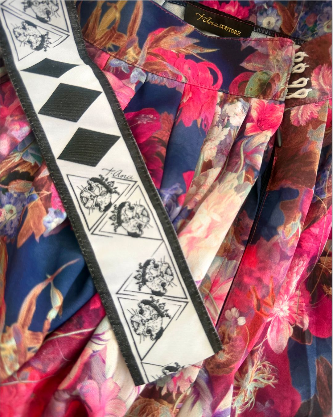 Luxury details of High-quality floral fabric detail showing print and texture of couture three-piece set; a floral satin couture set in blush and fuchsia tones by t•Ana Couture; captured under Mediterranean sunlight with divine flow and effortless elegance. Designer logos close-up details.