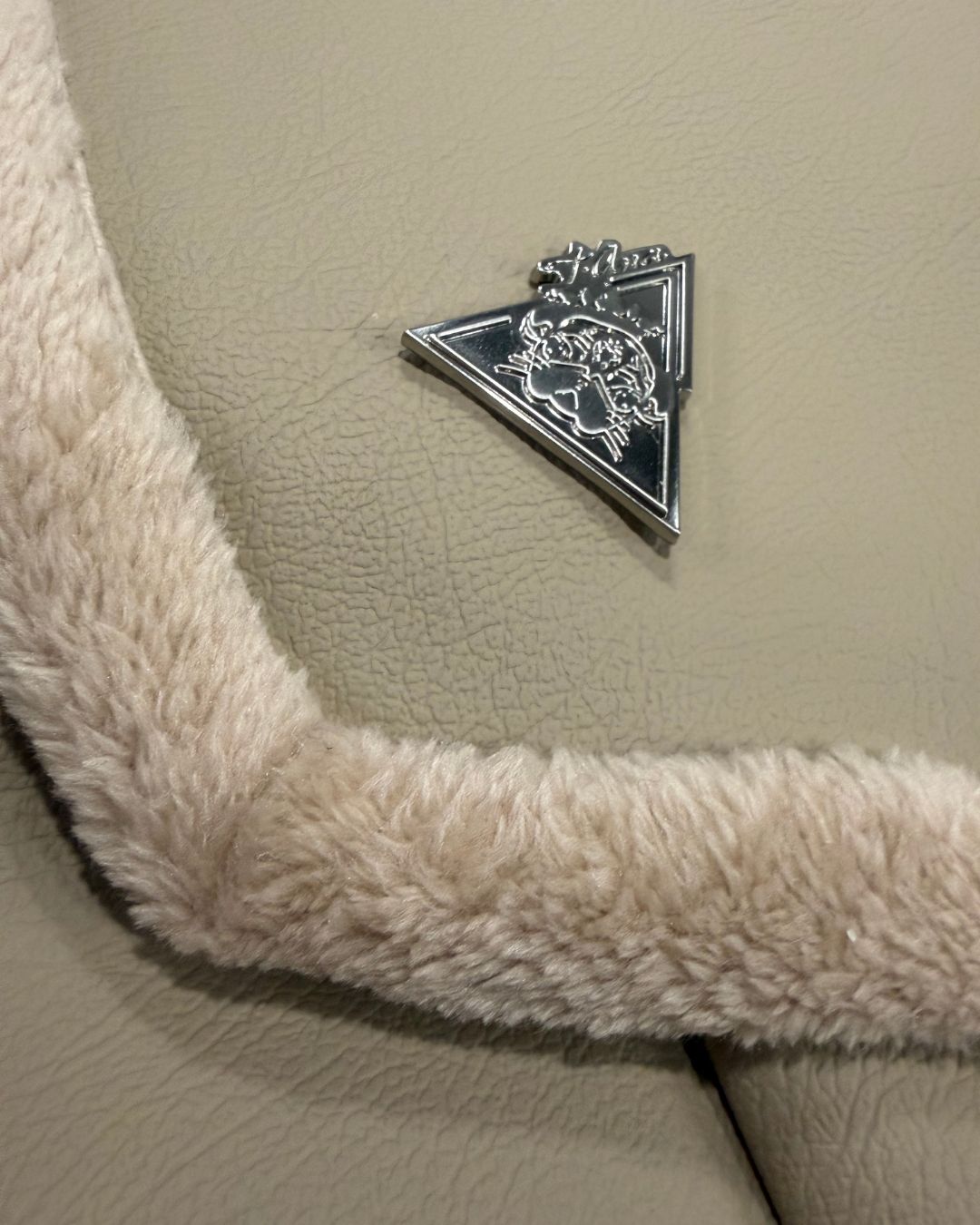 Silver t•Ana Couture logo plate on Amara Sabbia beige vegan leather clutch bag with faux-fur trim; Eternal Bond Series detail
