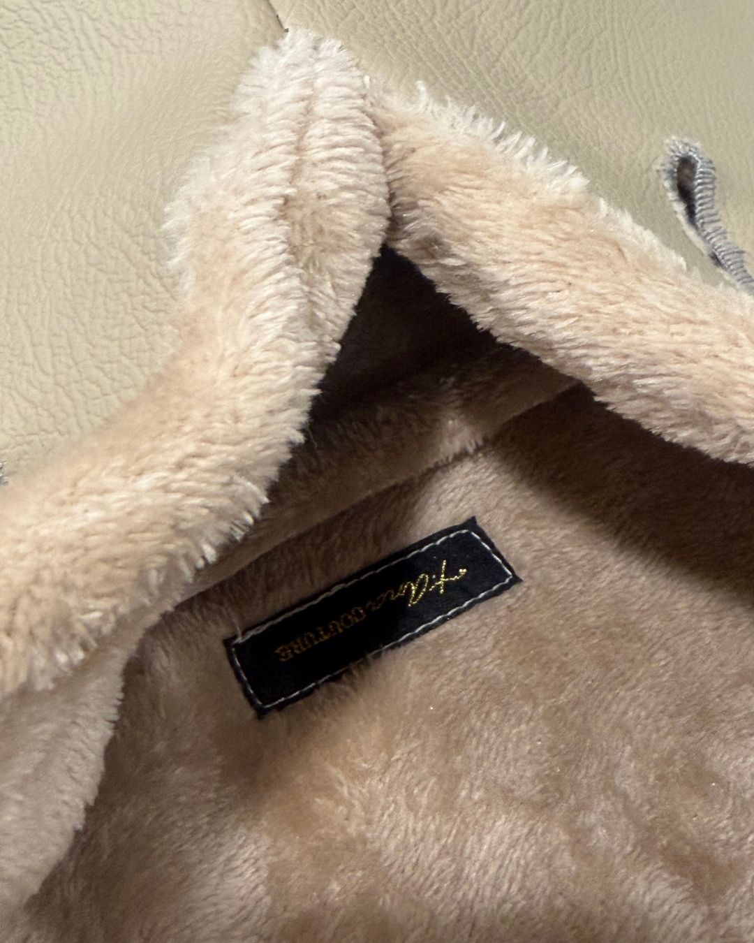Close-up of a plush beige fabric with a brand label. luxury lifestyle. Amara Sabbia Petite clutch handbag in beige vegan leather with and soft faux-fur trim with belt strap or handle holes; Mediterranean Muse Eternal Bond Series by t•Ana Couture.