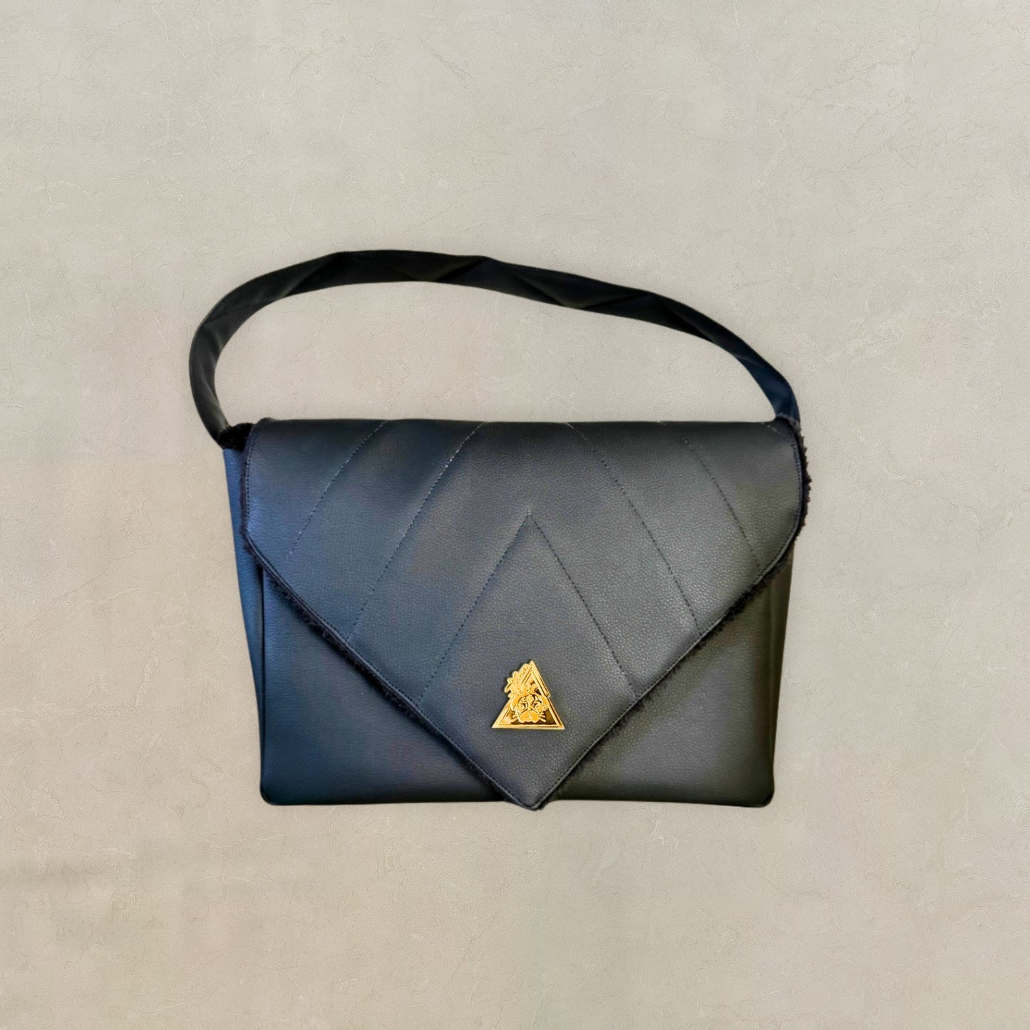 Front view of the t•Ana Couture El Clásica Elysian Eclipse CarryAll Mini handbag crafted in premium black vegan leather with architectural envelope flap, structured silhouette, and gold-tone signature emblem; Mediterranean luxury handbag handcrafted in Cyprus.