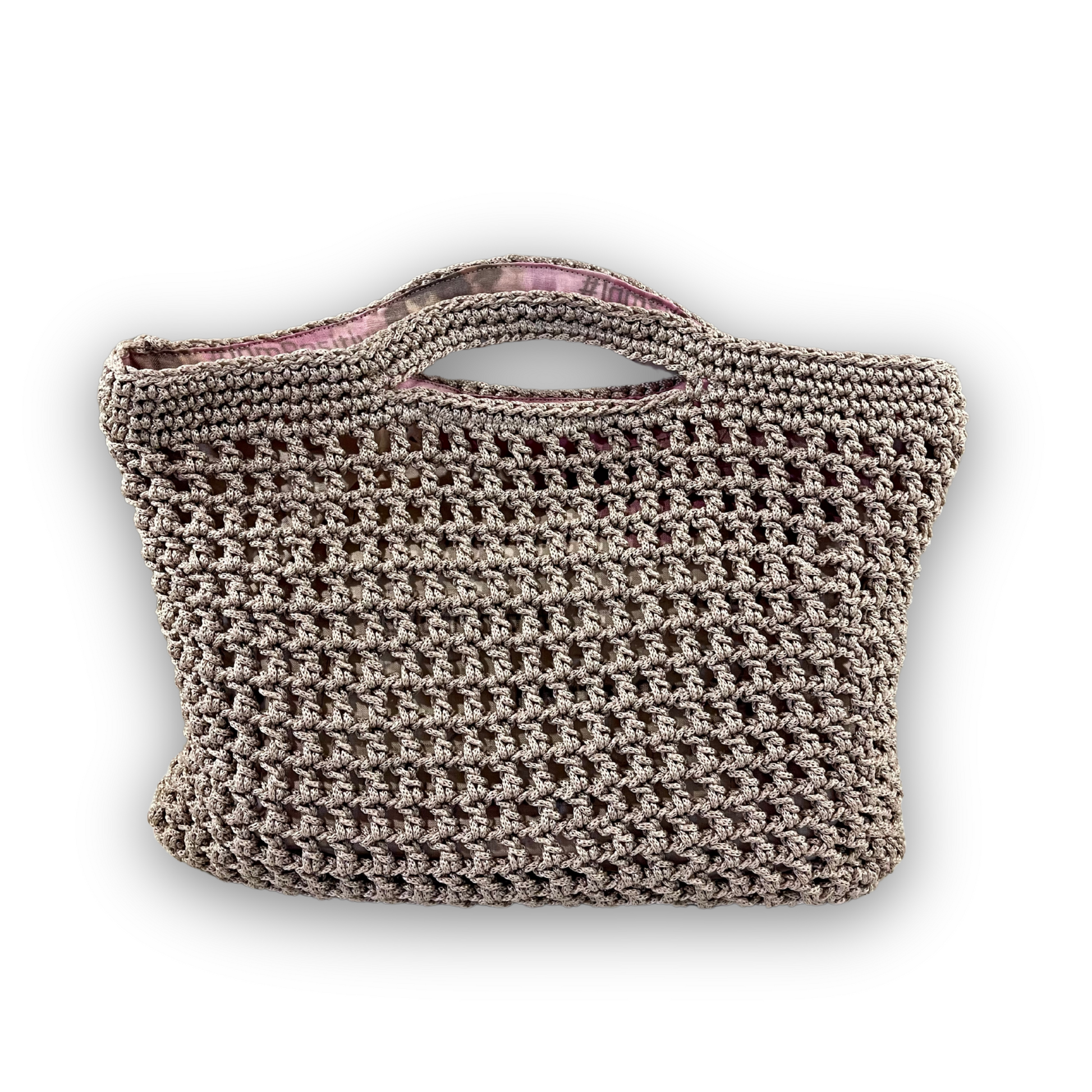 Crocheted handbag with a brand logo held over a branded surface. Mystic Mocha Bloom hand knit mocha handbag by t.Ana Couture; artisan crafted beige grey knit bag with organic linen zinnia floral lining from Mediterranean Muse Sand and Sea Collection