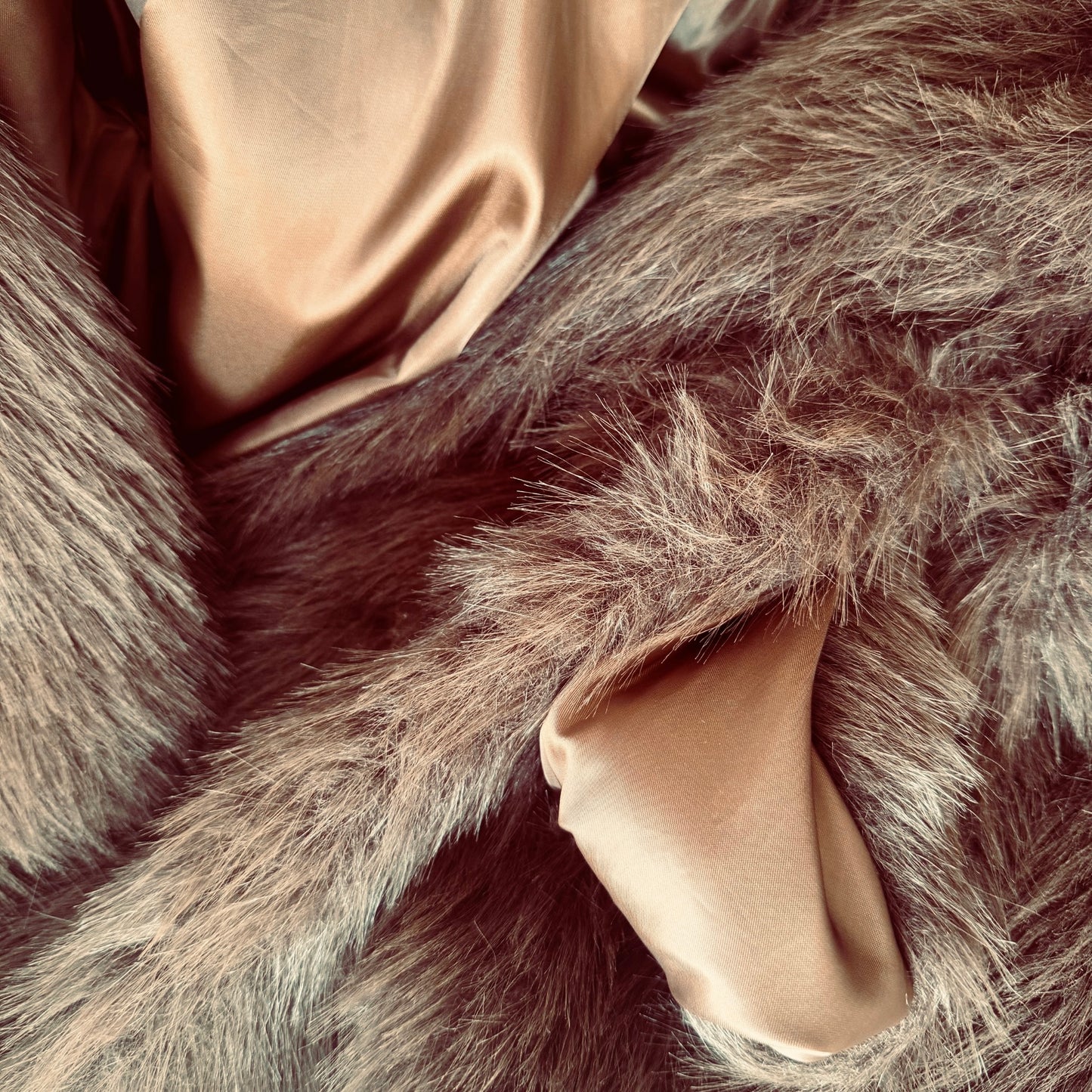Soft brown faux fur coat featuring natural wooden buttons and practical pockets; a plush, cosy and elegant neutral outerwear piece for women, designed for slow luxury winter styling and refined day to evening looks. This warm, timeless coat elevates everyday outfits with texture, comfort and effortless sophistication. Close up of faux fur and smooth lining.