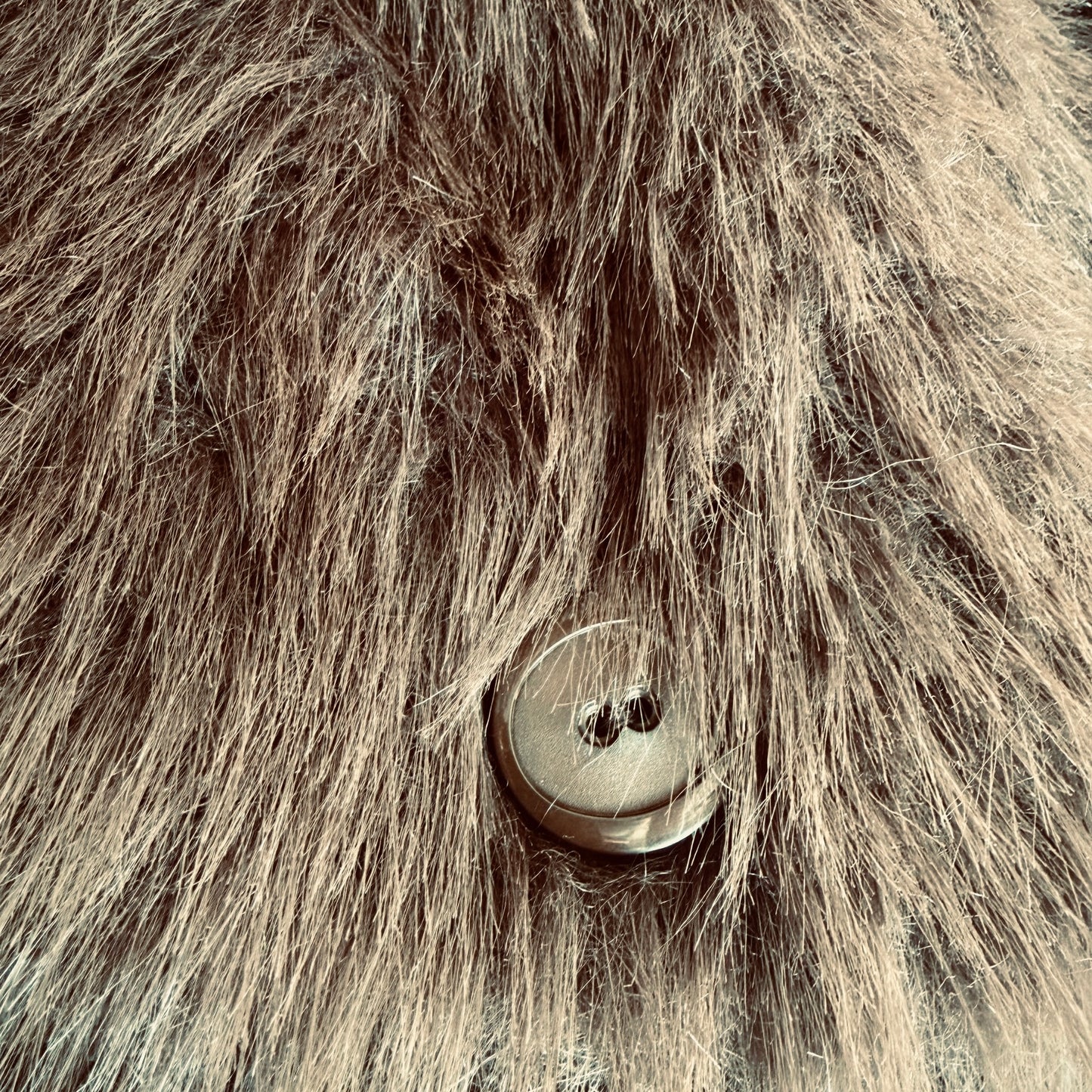 Soft brown faux fur coat featuring natural wooden buttons and practical pockets; a plush, cosy and elegant neutral outerwear piece for women, designed for slow luxury winter styling and refined day to evening looks. This warm, timeless coat elevates everyday outfits with texture, comfort and effortless sophistication. Close up of wooden button.