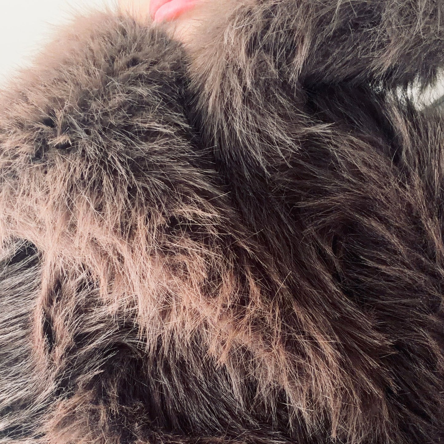 Soft brown faux fur coat featuring natural wooden buttons and practical pockets; a plush, cosy and elegant neutral outerwear piece for women, designed for slow luxury winter styling and refined day to evening looks. This warm, timeless coat elevates everyday outfits with texture, comfort and effortless sophistication. Close-up of faux fur.