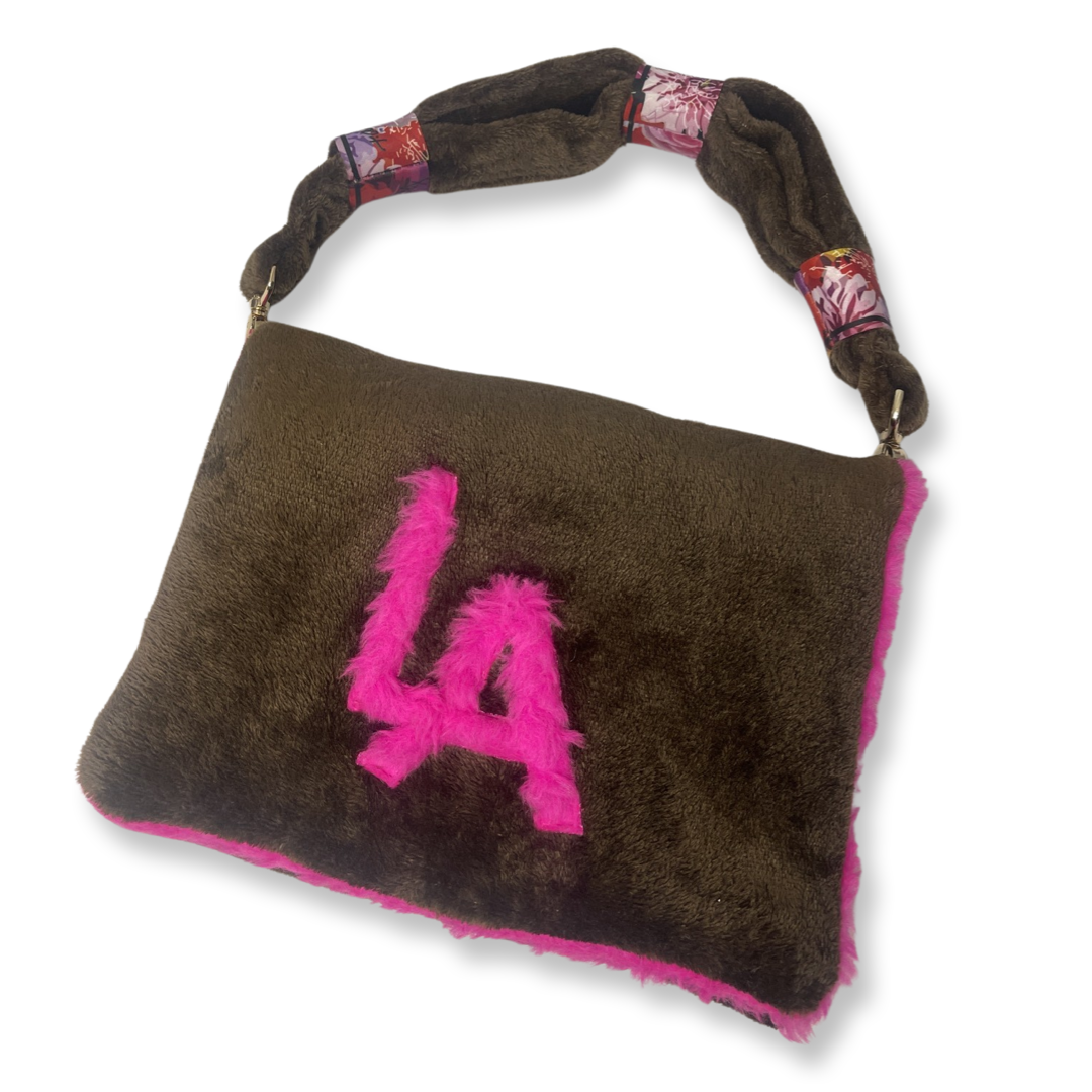 t•Ana Couture LA SnugglePlush Elegante handbag in brown faux fur with bold pink plush trim and LA lettering; luxury statement clutch styled with cream coat; sustainable upcycled design with modern street-luxe elegance.