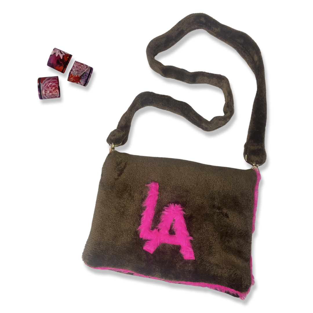 t•Ana Couture LA SnugglePlush Elegante handbag in brown faux fur with bold pink plush trim and LA lettering; luxury statement clutch styled with cream coat; sustainable upcycled design with modern street-luxe elegance.
